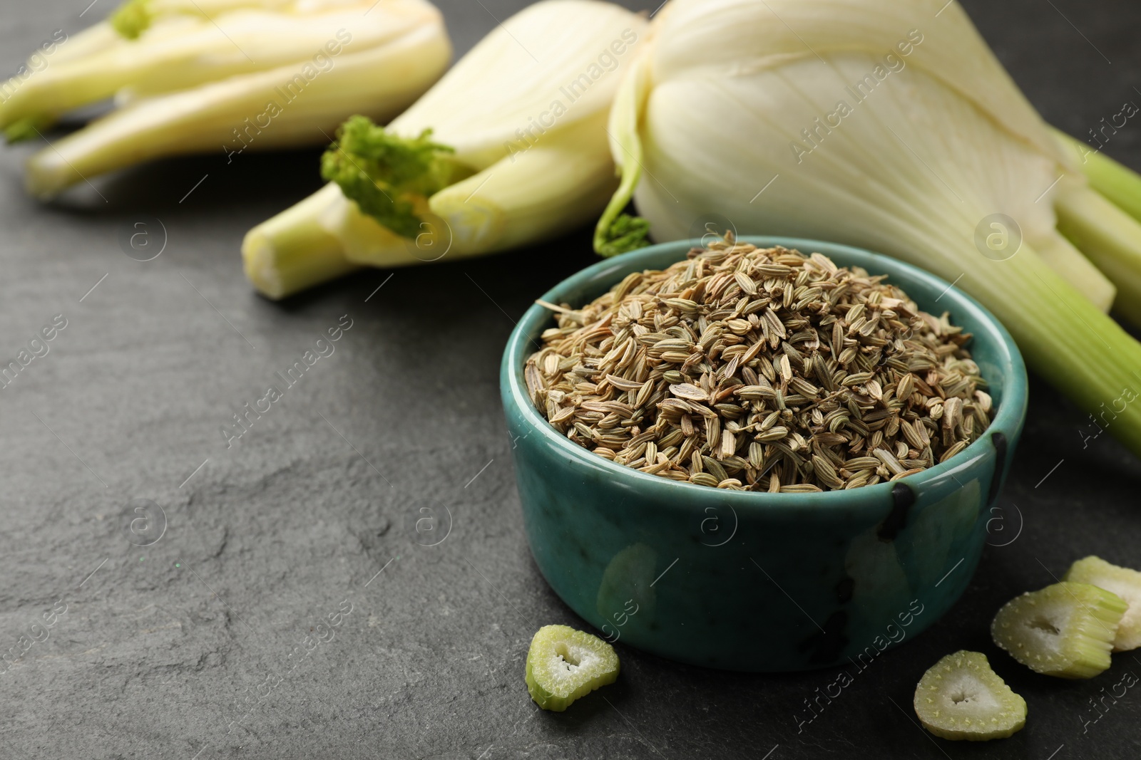 Photo of Fennel seeds in bowl, whole and cut vegetables on gray table, closeup. Space for text