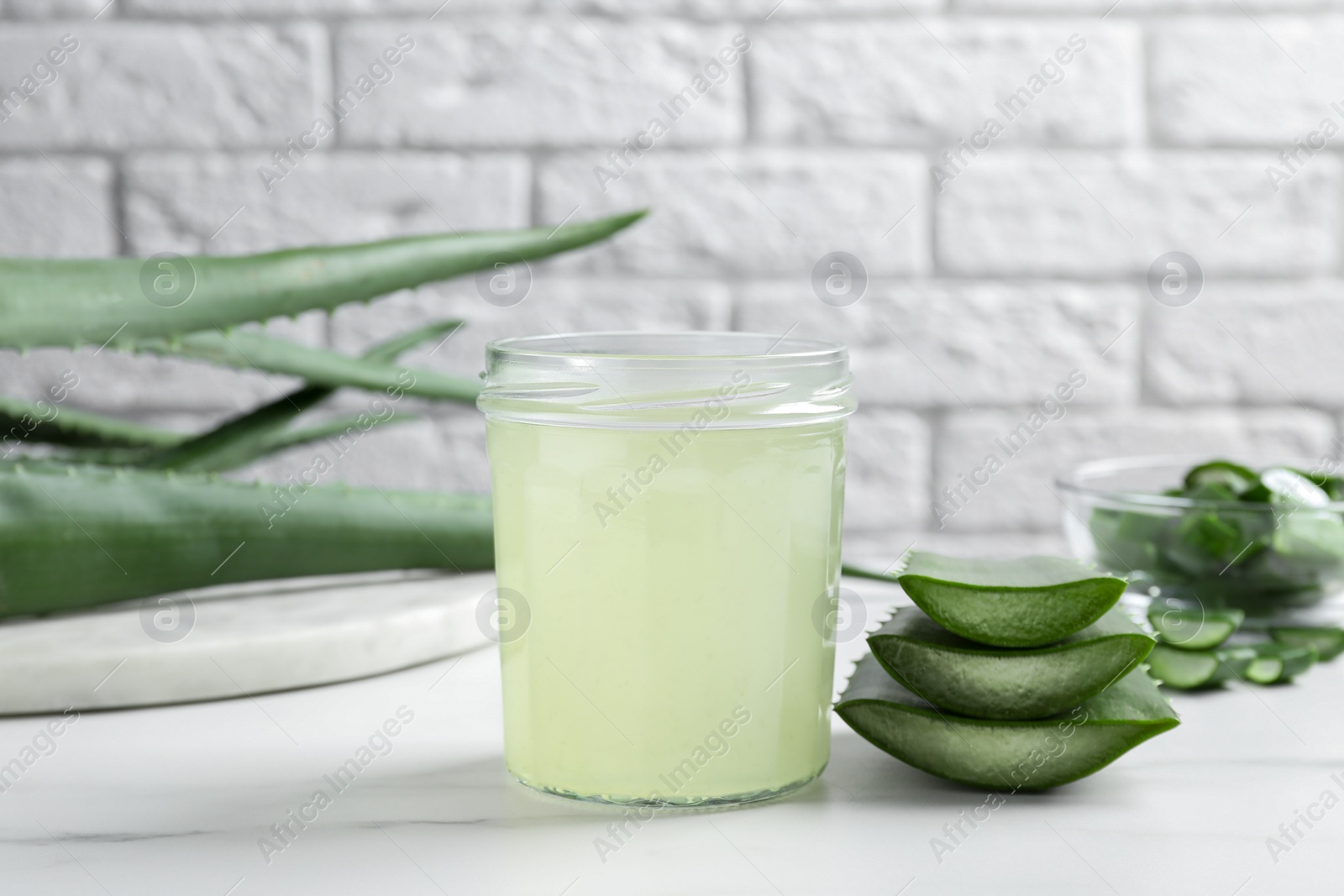 Photo of Fresh aloe juice in jar and leaves on white marble table, closeup