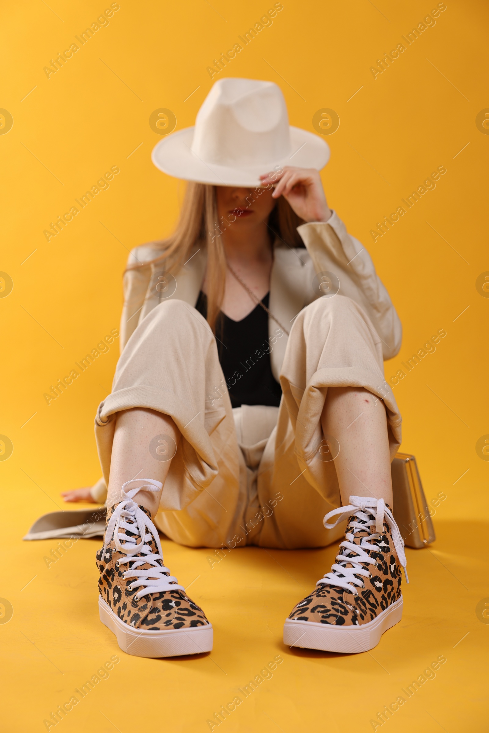 Photo of Stylish woman posing in classic old school sneakers with leopard print on orange background, selective focus