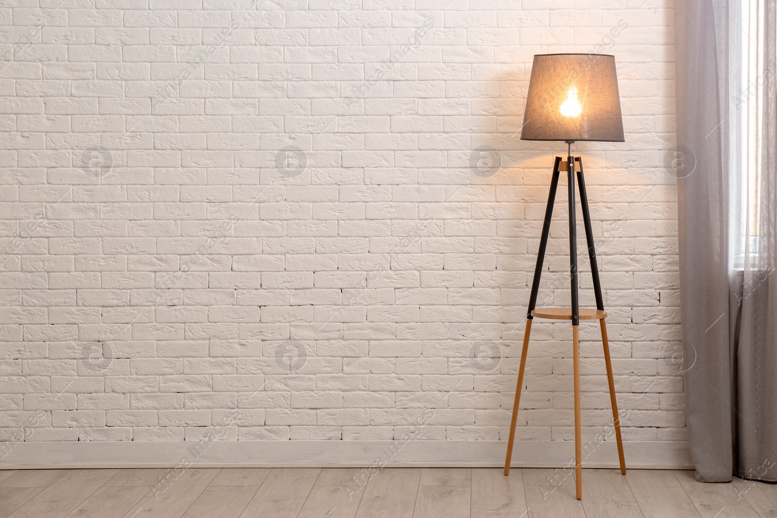 Photo of Modern floor lamp against brick wall indoors. Space for text
