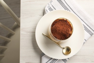 Photo of Delicious tiramisu in glass and spoon on white wooden table, top view