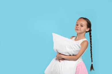Photo of Cute girl wearing pajamas with pillow on light blue background. Space for text