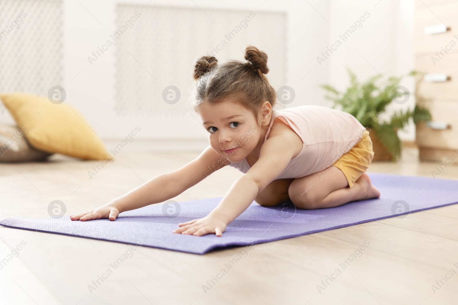 Photo of Little cute girl stretching herself on mat at home