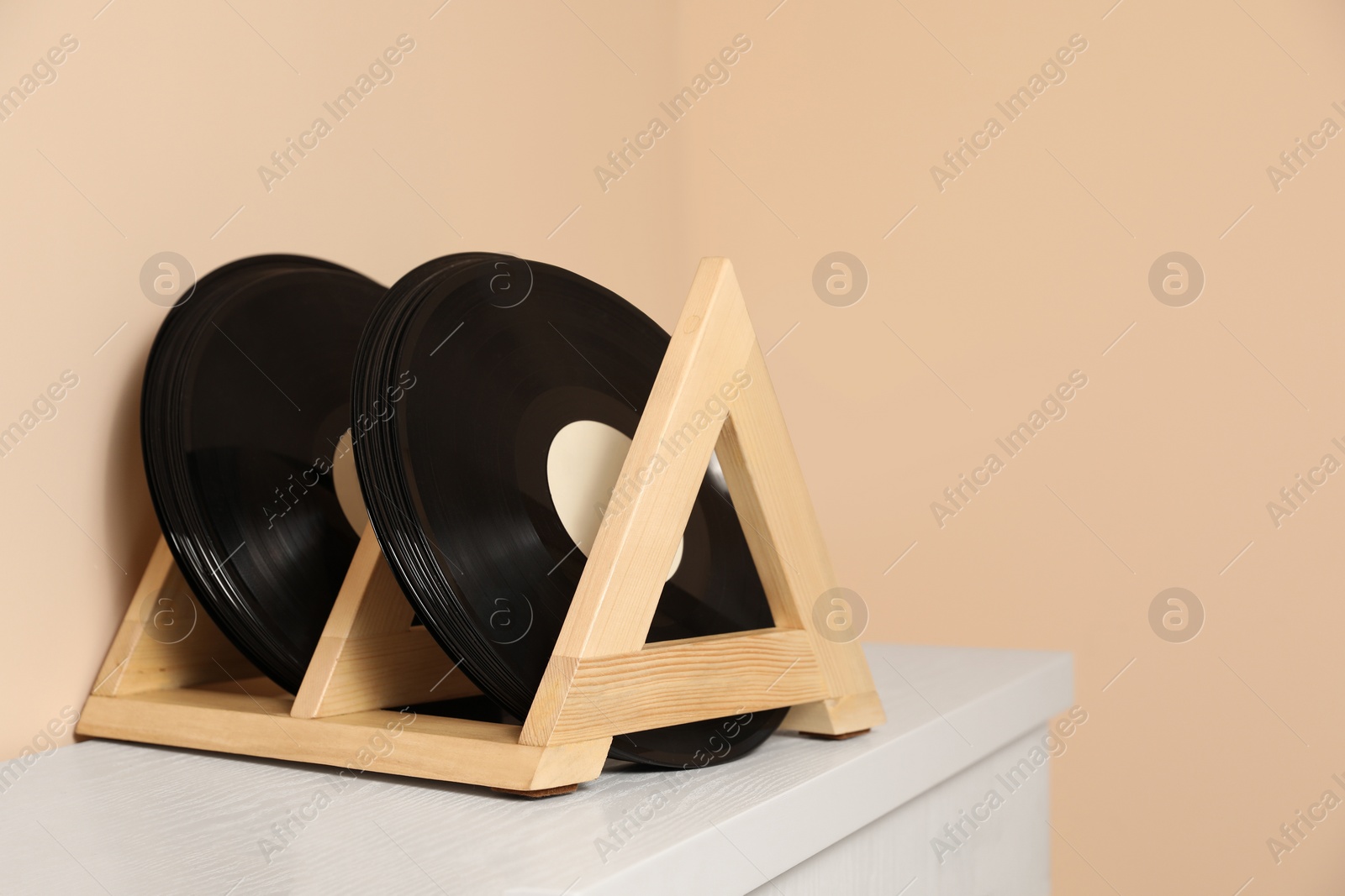 Photo of Vinyl records on white wooden drawer dresser near beige wall, space for text