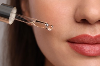 Young woman applying essential oil onto face, closeup