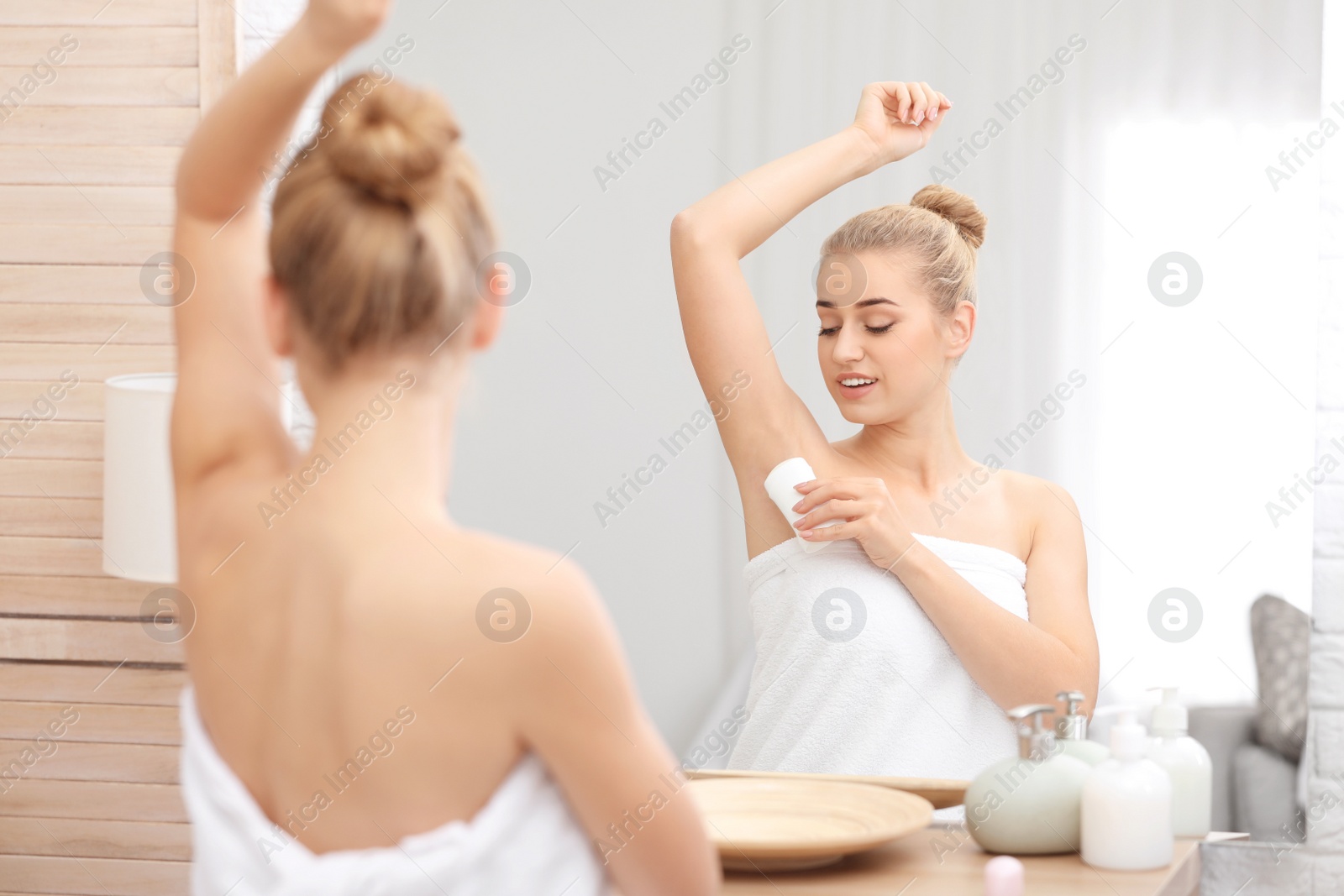 Photo of Beautiful young woman applying deodorant after shower in bathroom