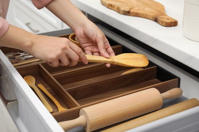 Photo of Woman putting wooden spatula into open drawerkitchen cabinet, closeup