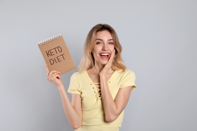 Photo of Woman holding notebook with phrase Keto Diet on grey background