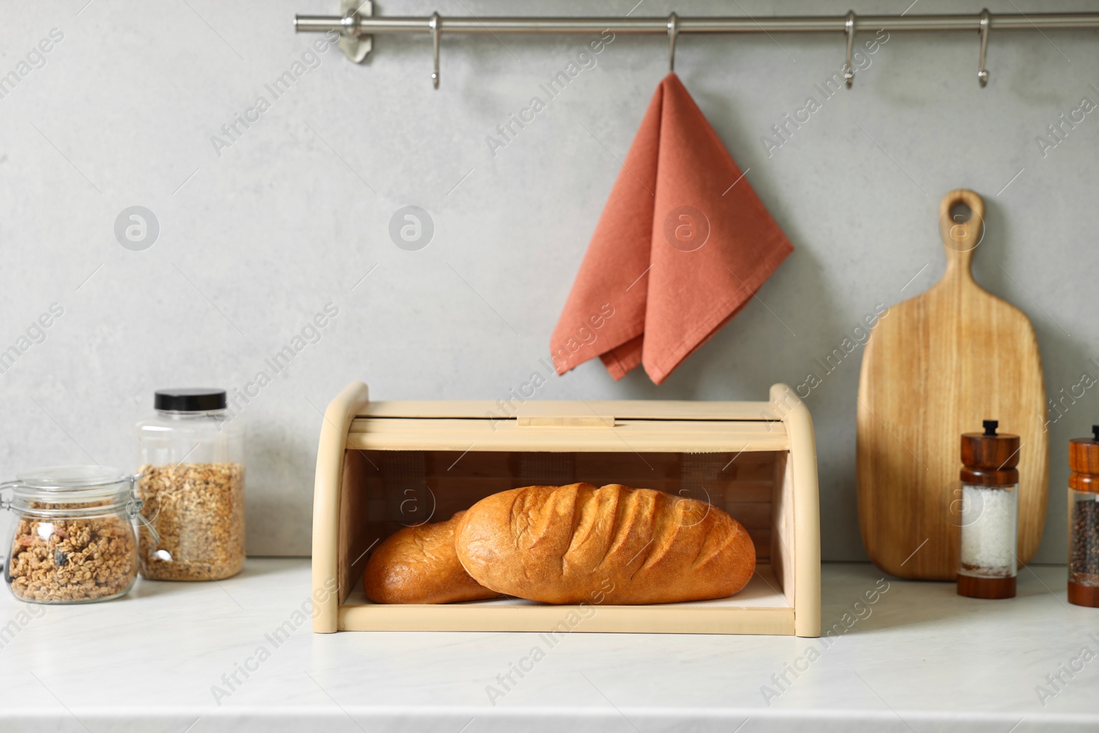 Photo of Wooden bread basket with freshly baked loaves on white marble table in kitchen