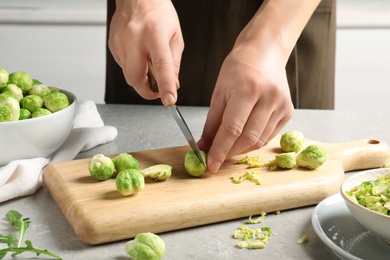 Photo of Woman cutting fresh Brussels sprouts on wooden board, closeup