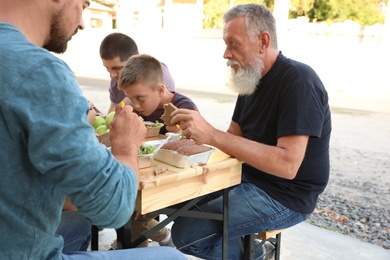 Photo of Poor people eating food at wooden table outdoors