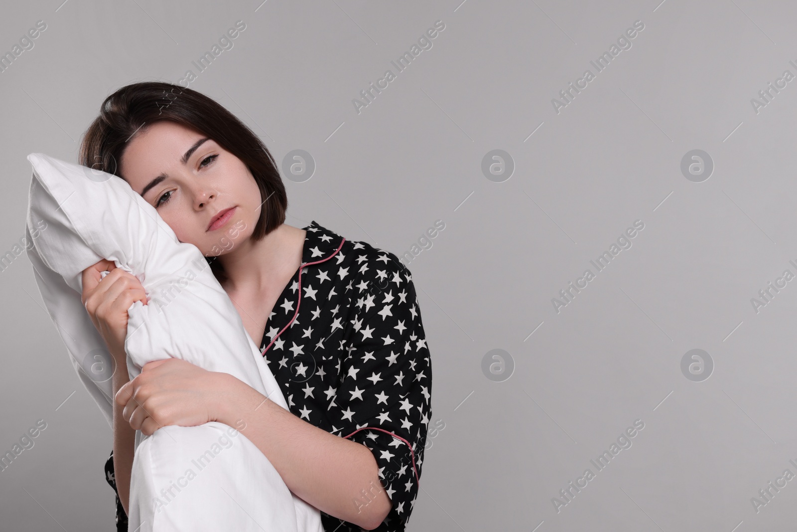 Photo of Unhappy young woman with pillow on light grey background, space for text. Insomnia problem