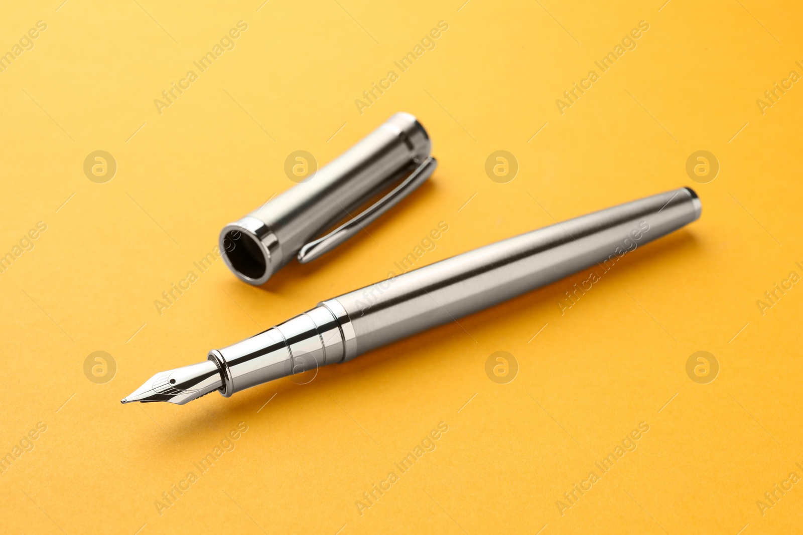 Photo of Stylish silver fountain pen with cap on yellow background