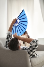 Photo of Man with hand fan lying on sofa. Summer season