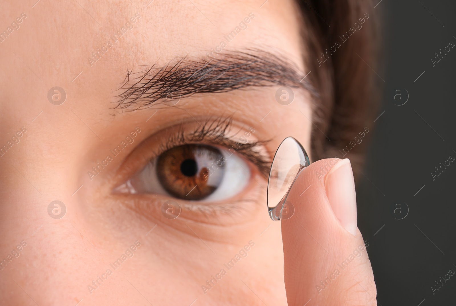 Photo of Young woman putting contact lens in her eye, closeup