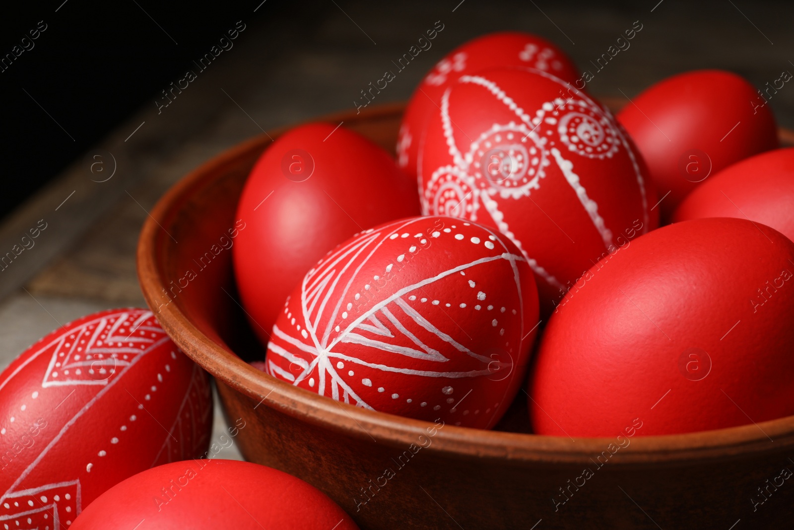 Photo of Wooden bowl with red painted Easter eggs on table, closeup