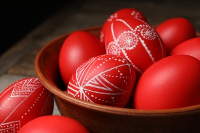 Wooden bowl with red painted Easter eggs on table, closeup