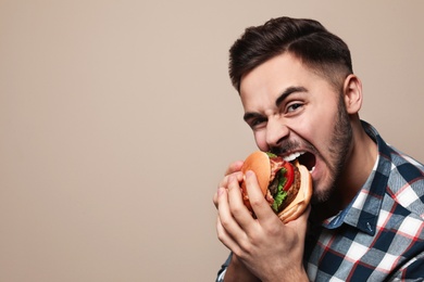 Photo of Handsome man eating tasty burger on color background. Space for text
