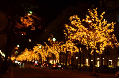 Photo of Blurred view of street with beautiful lights on trees and cars at night. Bokeh effect