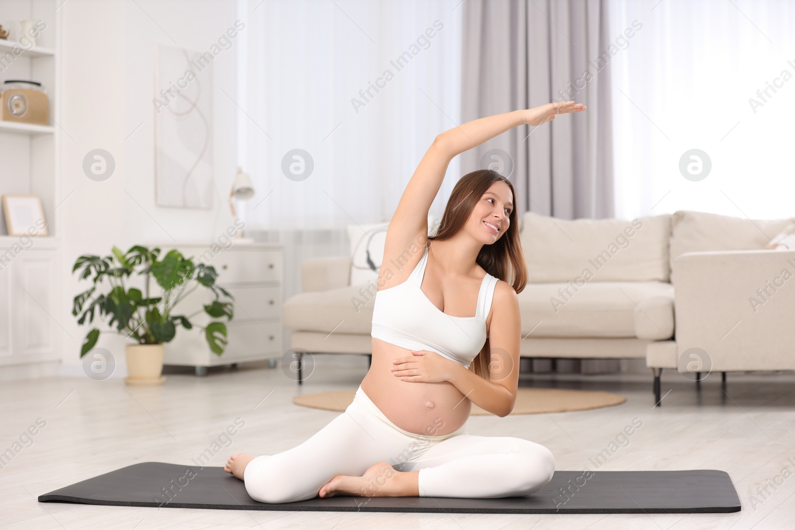 Photo of Pregnant woman doing exercises on yoga mat at home