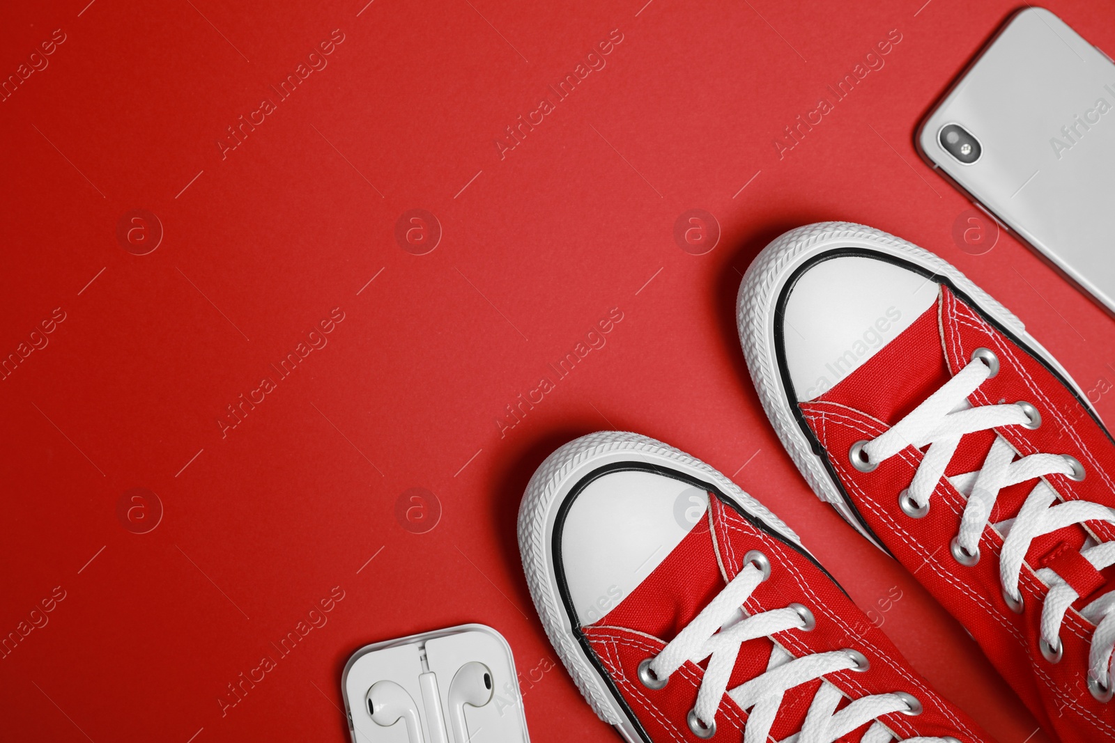 Photo of Pair of new stylish sneakers, smartphone and wireless earphones on red background, flat lay. Space for text