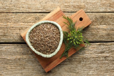 Photo of Board with bowl of dry seeds and fresh dill on wooden table, top view