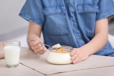 Cute girl eating tasty yogurt at table, closeup