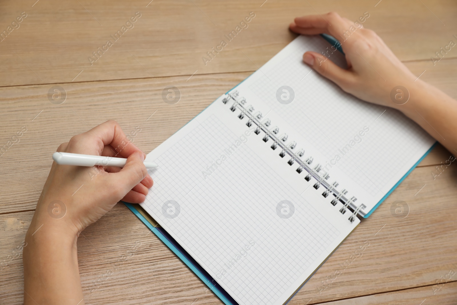 Photo of Left-handed woman writing in notebook at wooden table, closeup