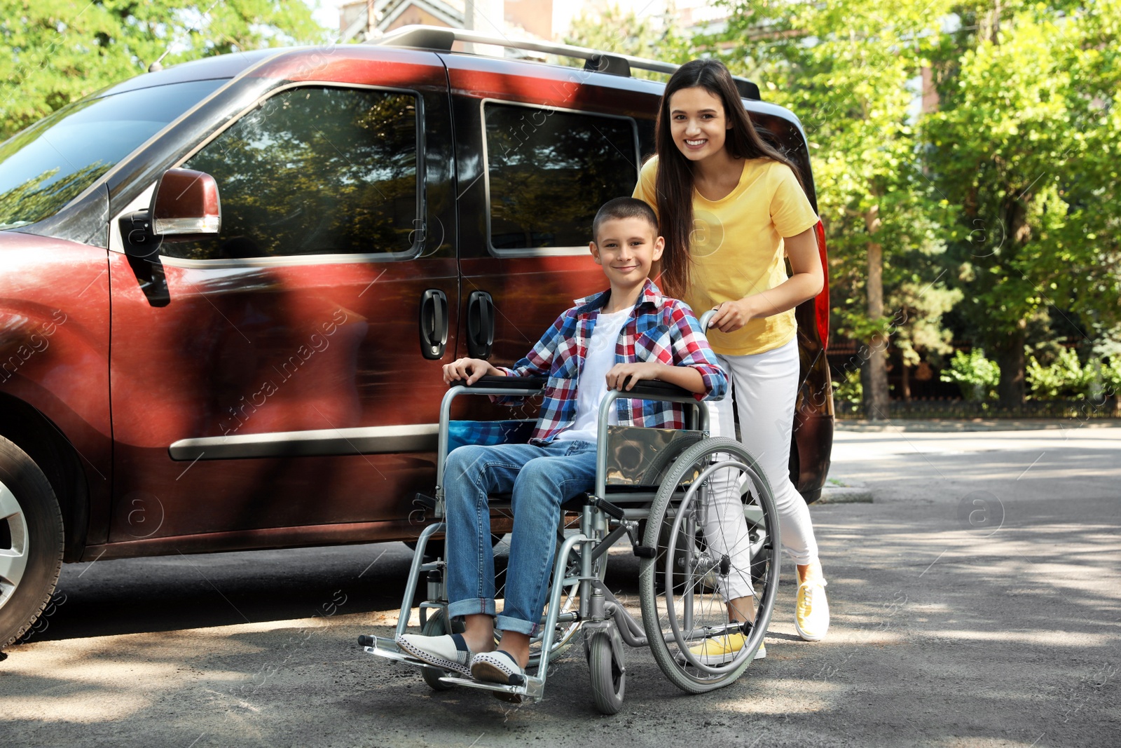 Photo of Young woman with boy in wheelchair near van outdoors