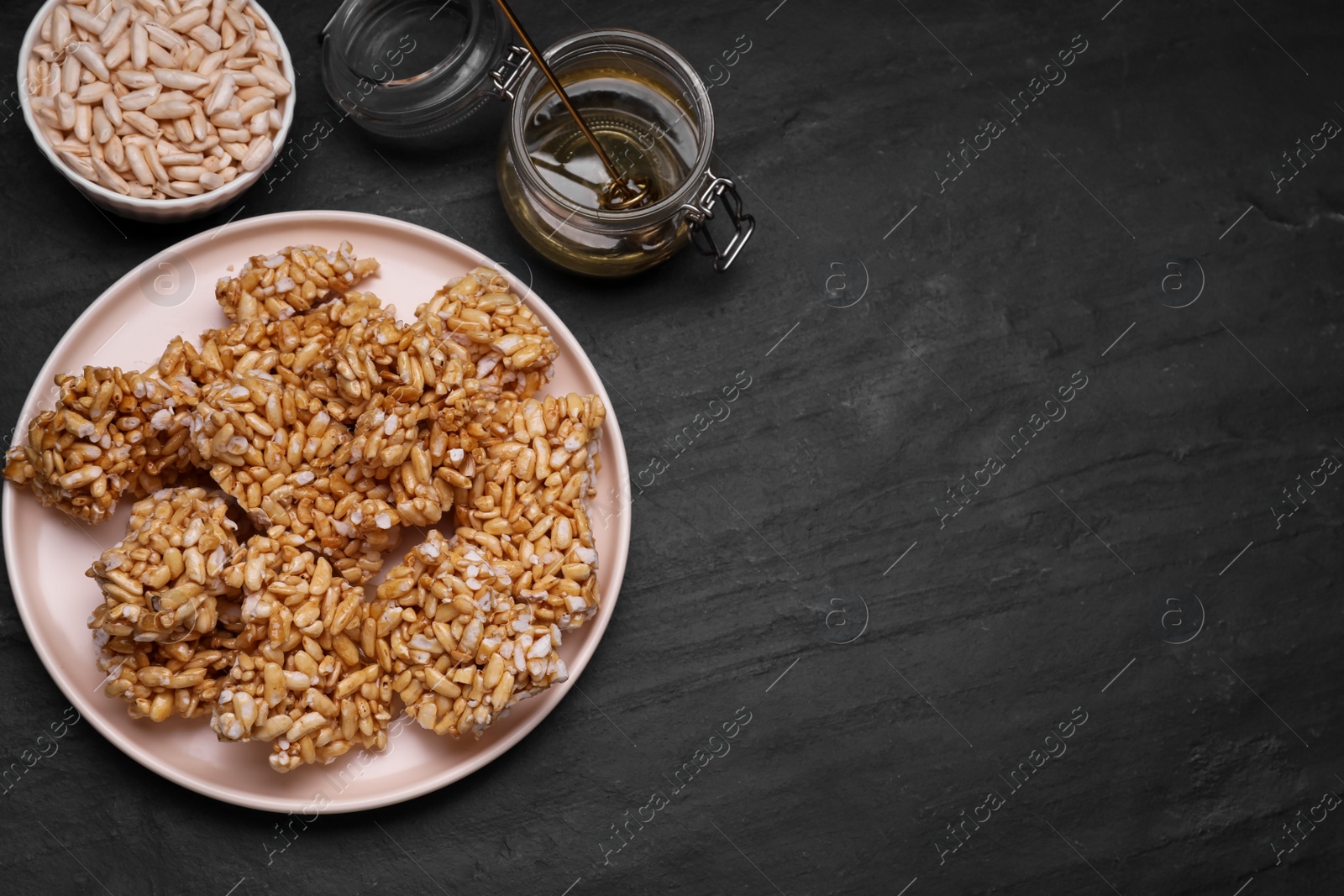 Photo of Puffed rice pieces (kozinaki) on black table, flat lay. Space for text