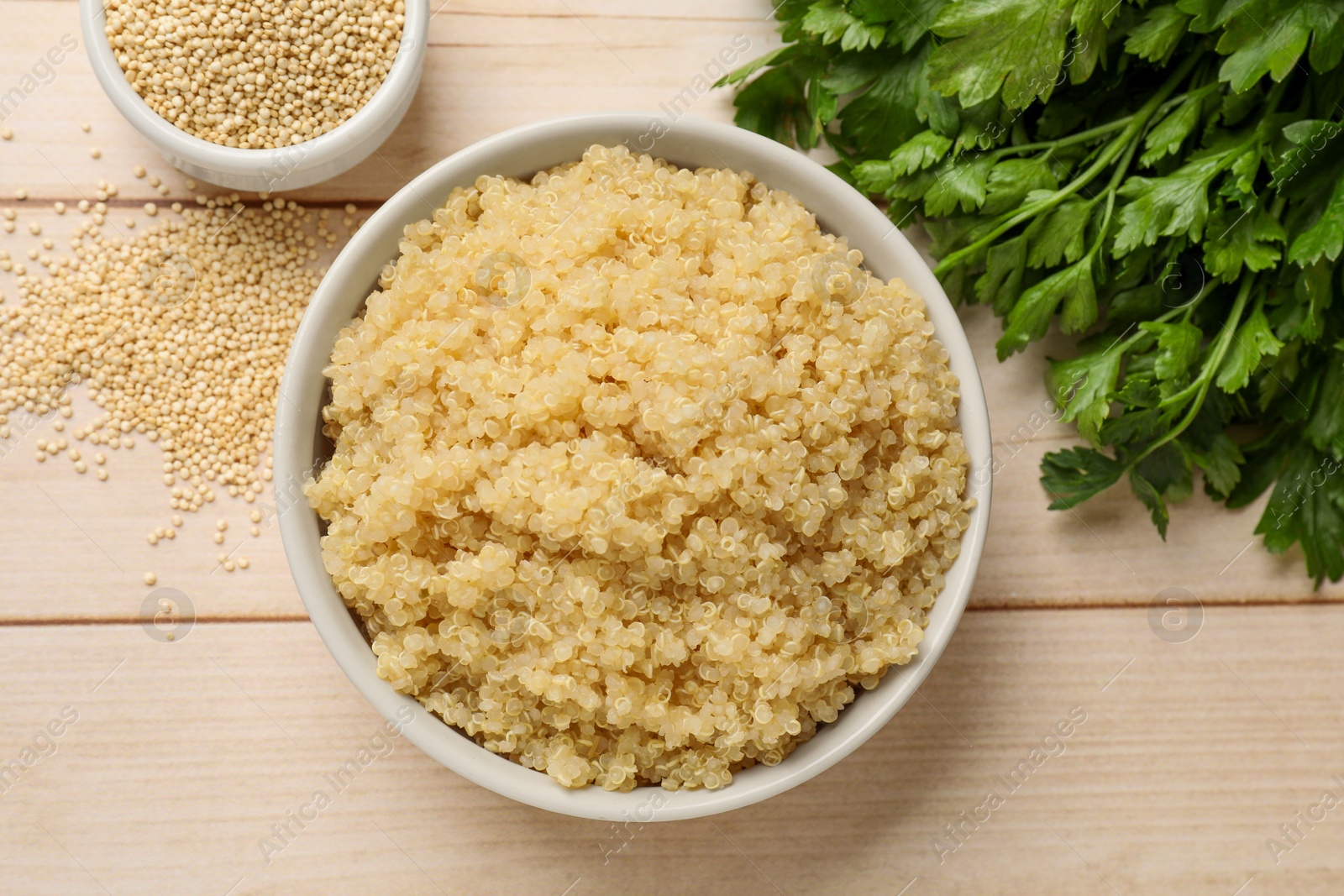 Photo of Tasty quinoa porridge in bowl, seeds and parsley on light wooden table, flat lay