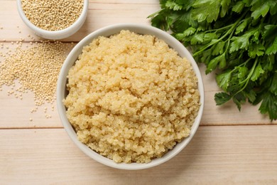 Photo of Tasty quinoa porridge in bowl, seeds and parsley on light wooden table, flat lay