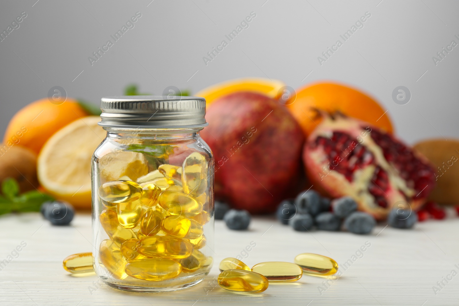 Photo of Vitamin pills in bottle and fresh fruits on white wooden table. Space for text