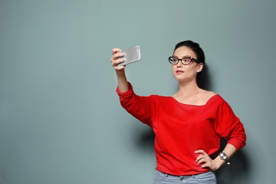 Attractive young woman taking selfie on grey background