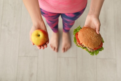 Photo of Woman holding tasty sandwich and fresh apple, top view. Choice between diet and unhealthy food