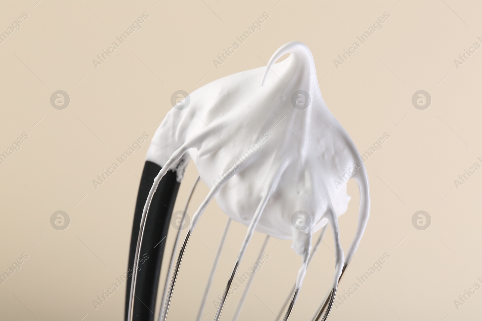 Photo of Whisk with whipped cream on beige background, closeup