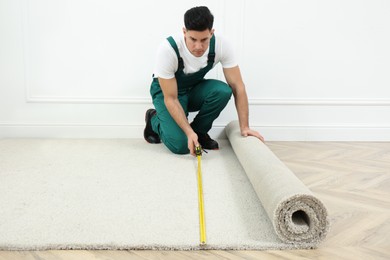 Photo of Worker with measuring tape installing new carpet indoors