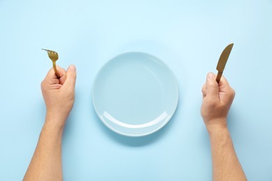 Photo of Man with cutlery and empty plate at light blue table, top view