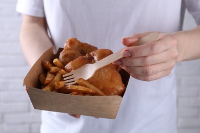 Photo of Woman eating fish and chips near white brick wall, closeup