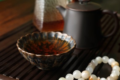 Cup with freshly brewed pu-erh tea and prayer beads on wooden tray, closeup