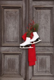 Photo of Pair of ice skates with Christmas decor hanging on old wooden door