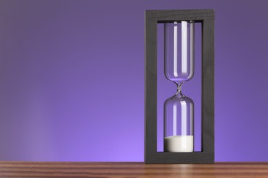 Photo of Hourglass with flowing sand on purple background. Space for text