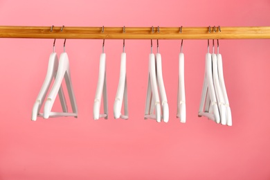 Photo of Empty clothes hangers on wooden rail against color background