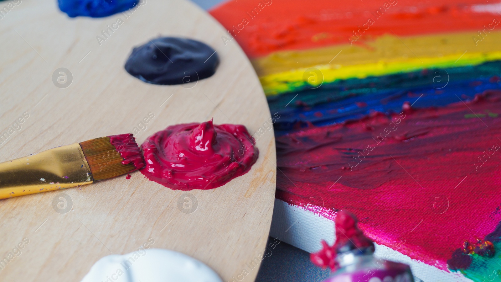 Photo of Artist's palette with colorful samples, brush and canvas with mixed bright paints, closeup