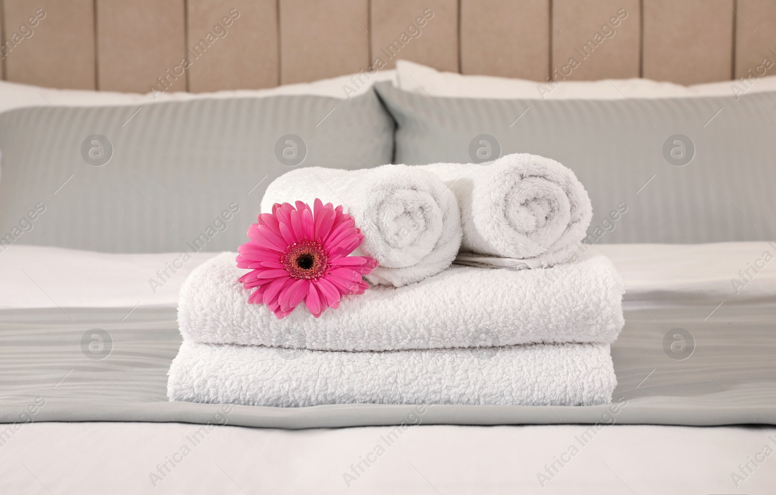 Photo of Fresh white towels with flower on bed indoors