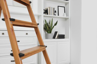 Wooden folding ladder near chest of drawers and shelf with accessories indoors