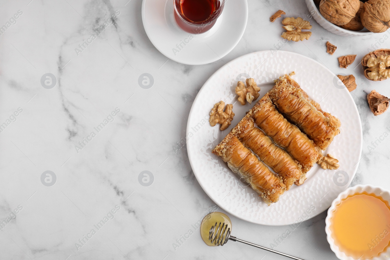 Photo of Eastern sweets. Pieces of tasty baklava, walnuts and tea on white marble table, flat lay. Space for text