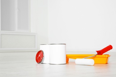 Photo of Cans of paint and decorator tools on wooden floor indoors