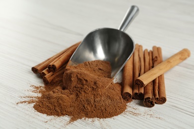 Photo of Aromatic cinnamon powder and sticks on white table, closeup