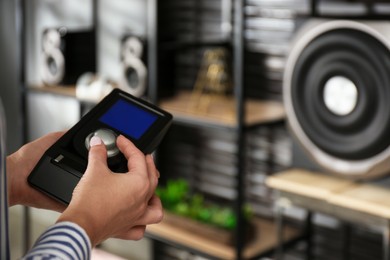 Photo of Woman using remote to control audio speaker system indoors, closeup